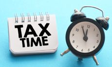 TAX TIME words in a notebook next to an alarm clock on a blue background.