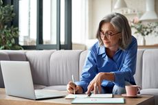 A woman writes while looking at a computer screen. 