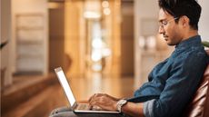 A man sits in the hallway of a fancy office building with his laptop open on his lap.