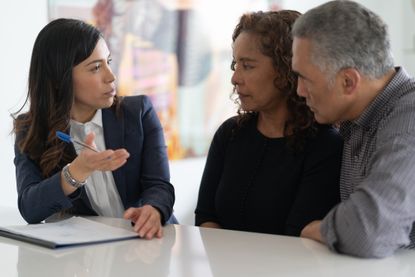 A Latino couple is in a meeting with their financial advisor. They are devising a financial plan at their kitchen table.