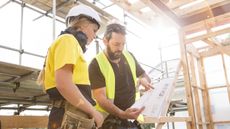 A woman and man wearing hard hats look at blueprints in a house that's being built.